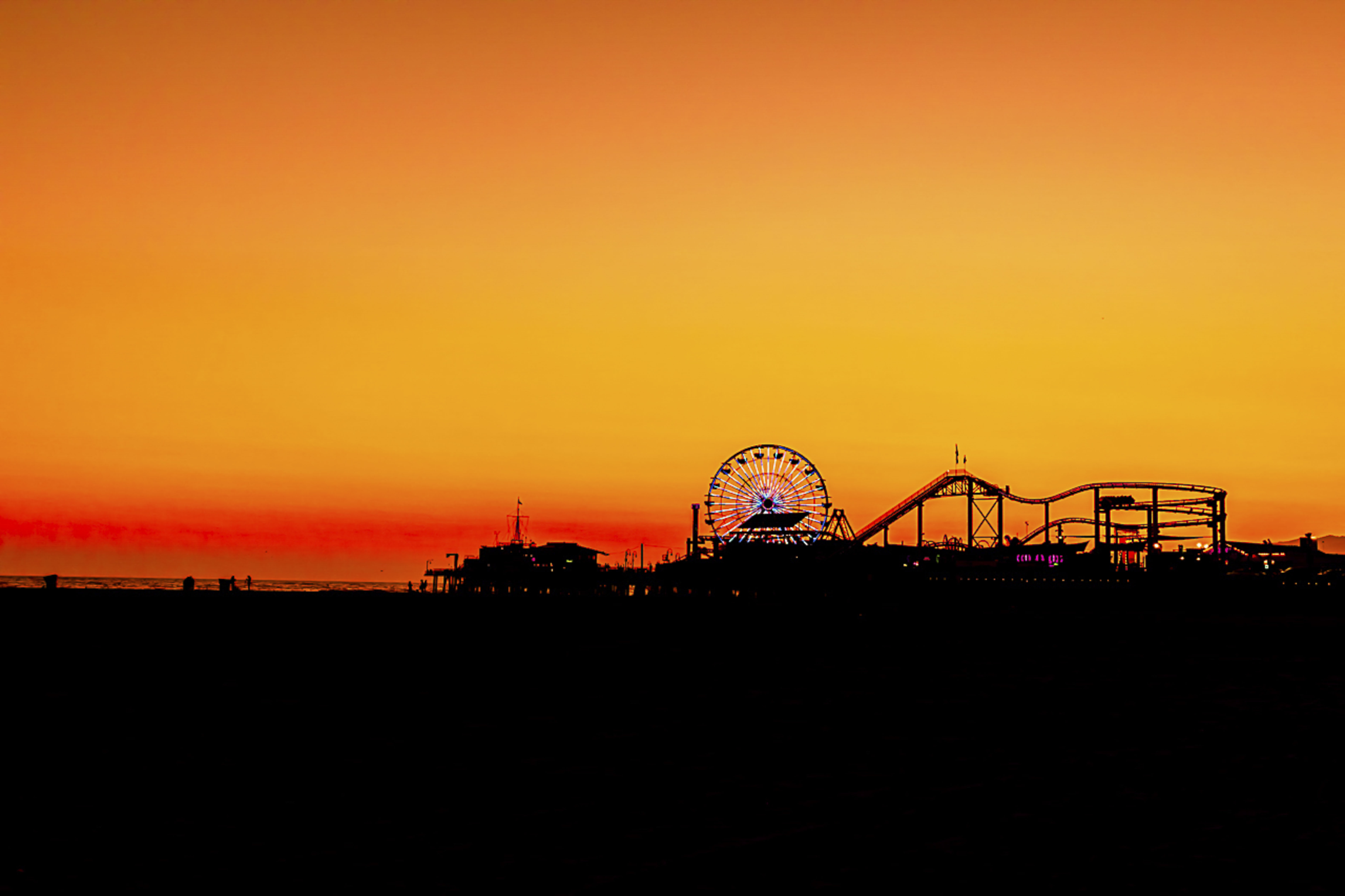 Santa Monica Pier at sunset — Ferris wheel and roller coaster silhouetted against a blazing orange sky