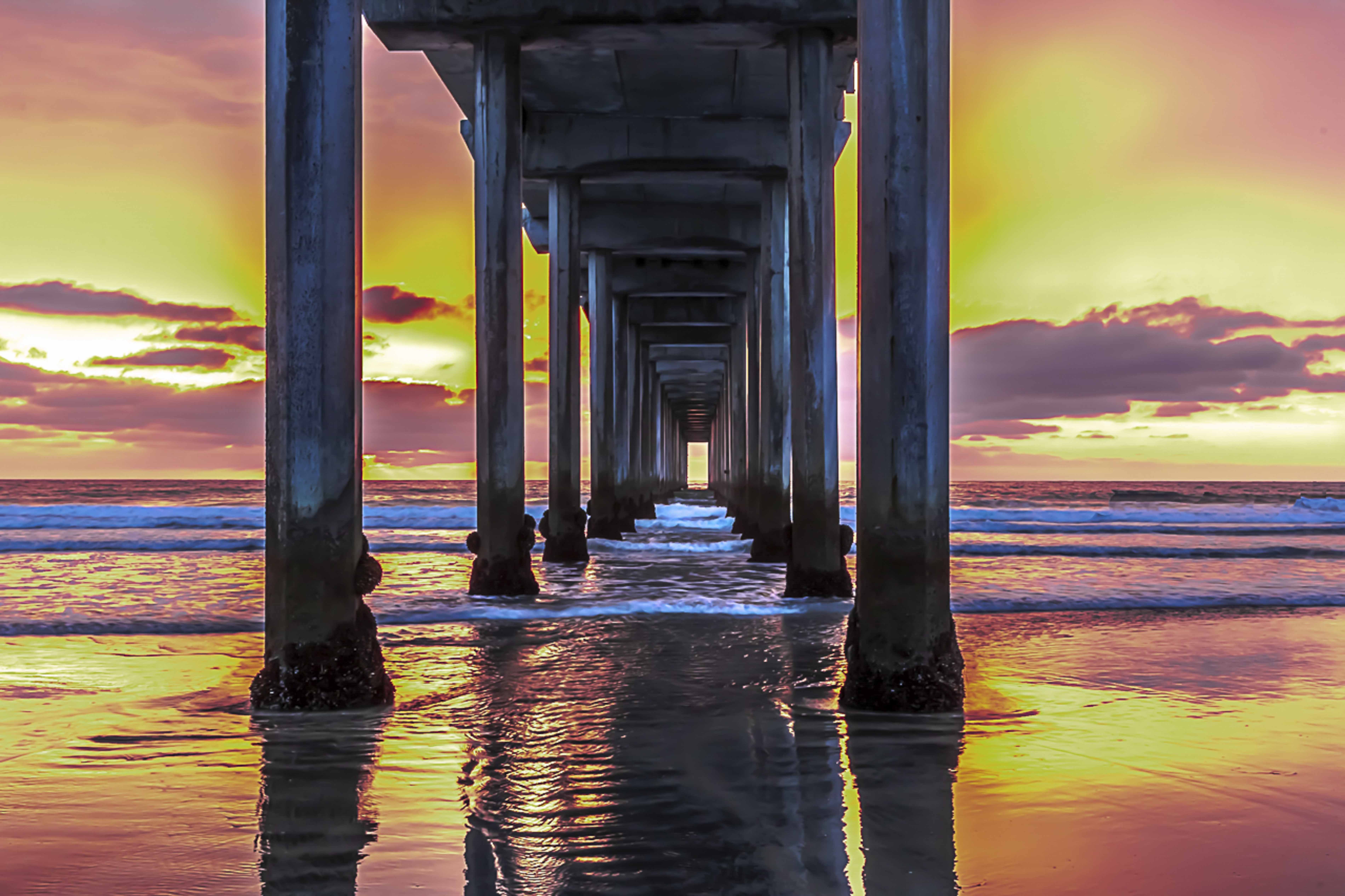 Symmetrical view straight under the pier at sunset, columns reflecting in the wet sand