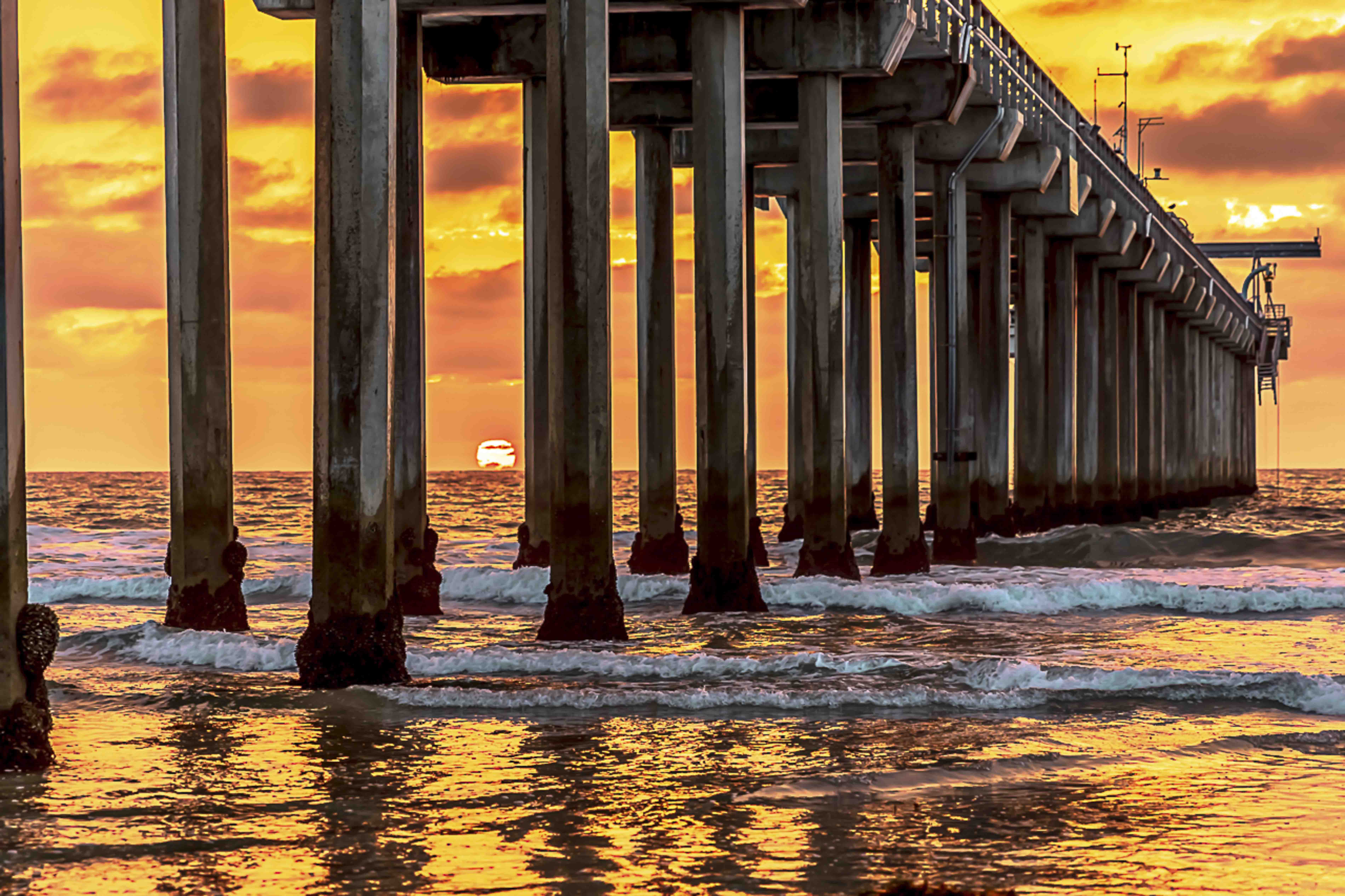 Pier columns at golden hour, sun setting low over the Pacific