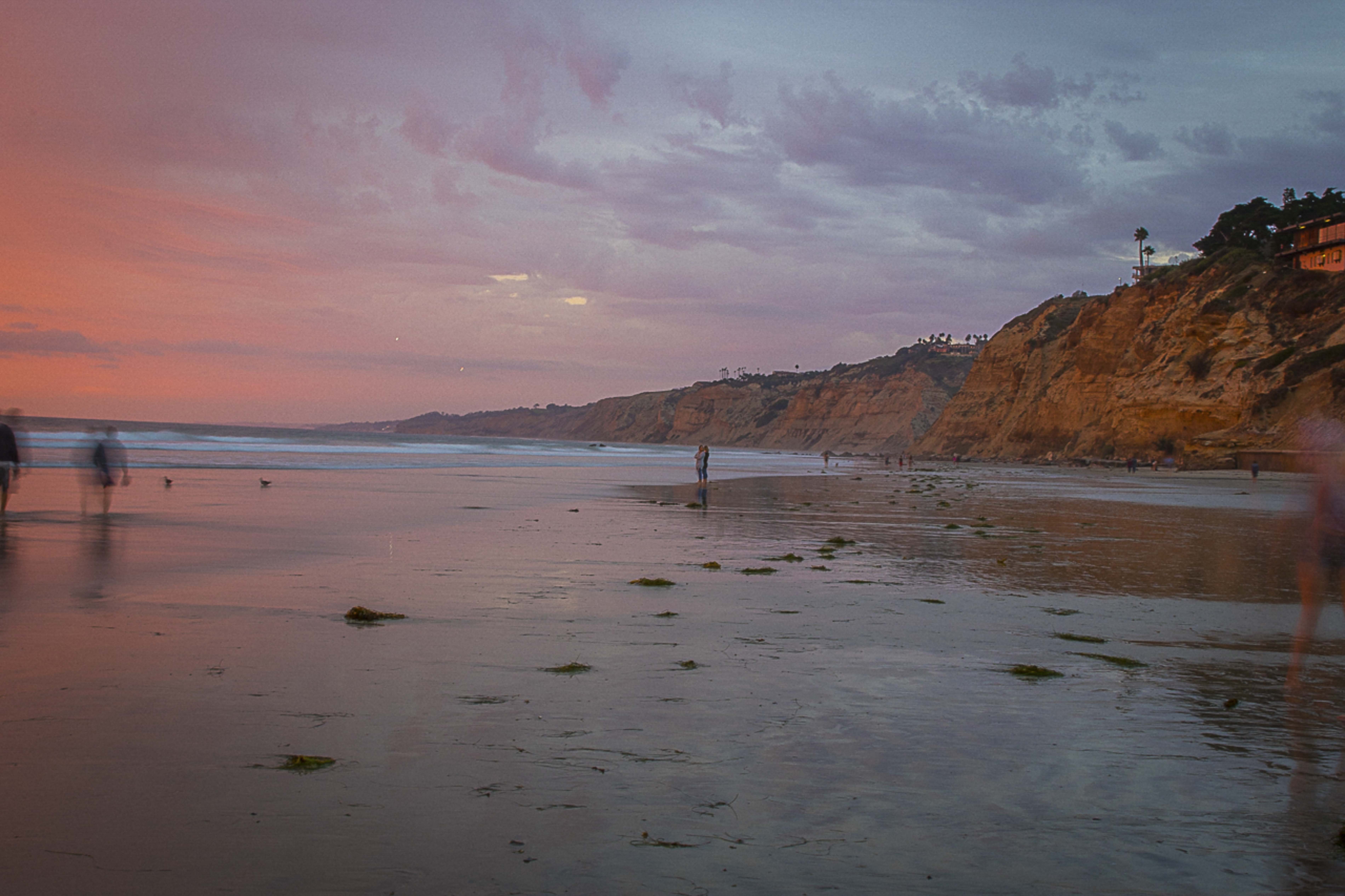 Pink and purple beach sunset with sea cliffs and silhouetted beachgoers