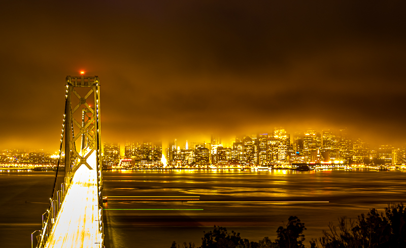 Bay Bridge tower at night — vertical cables glowing against a deep blue sky