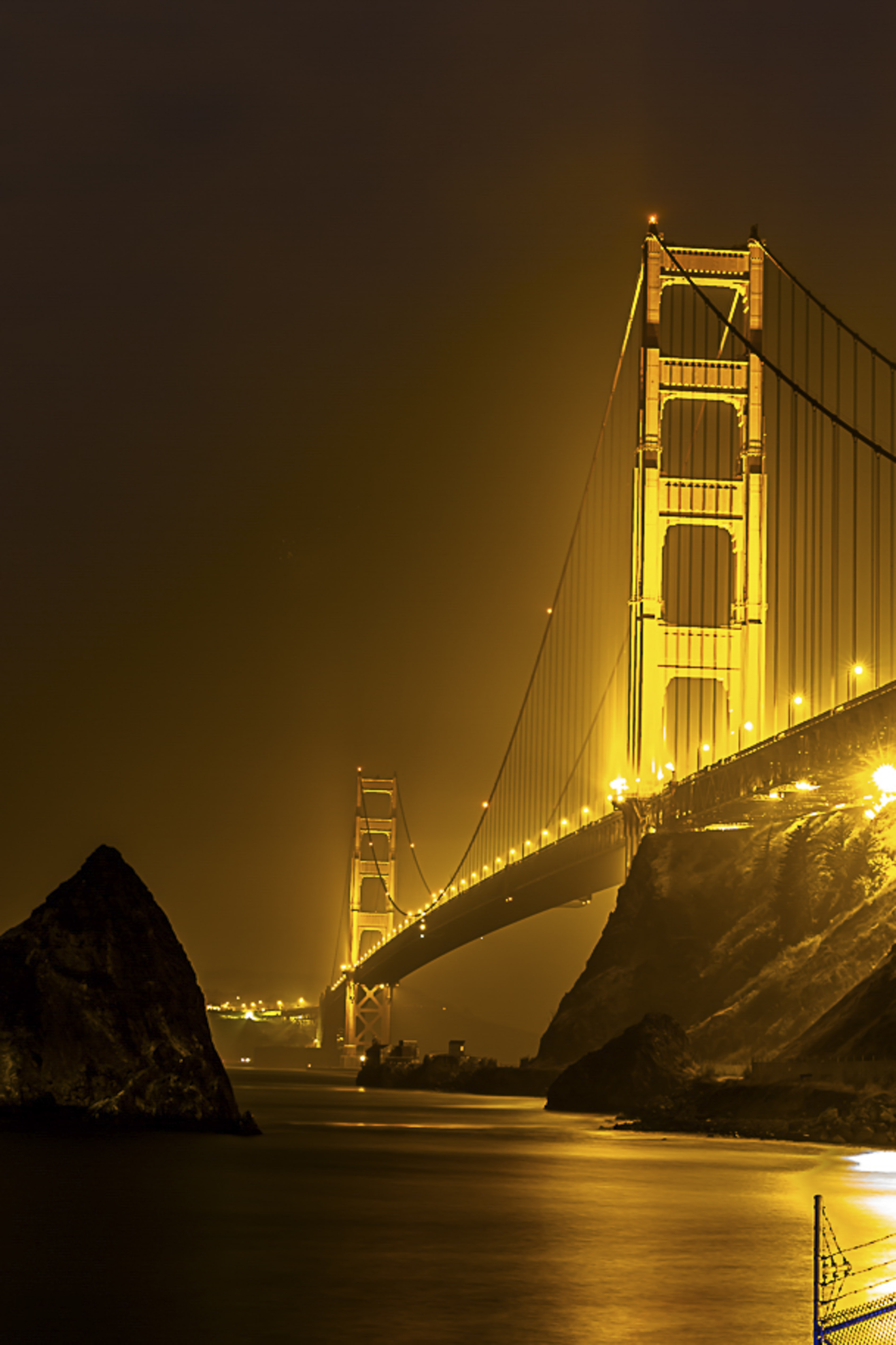 Golden Gate Bridge glowing gold through the fog at night
