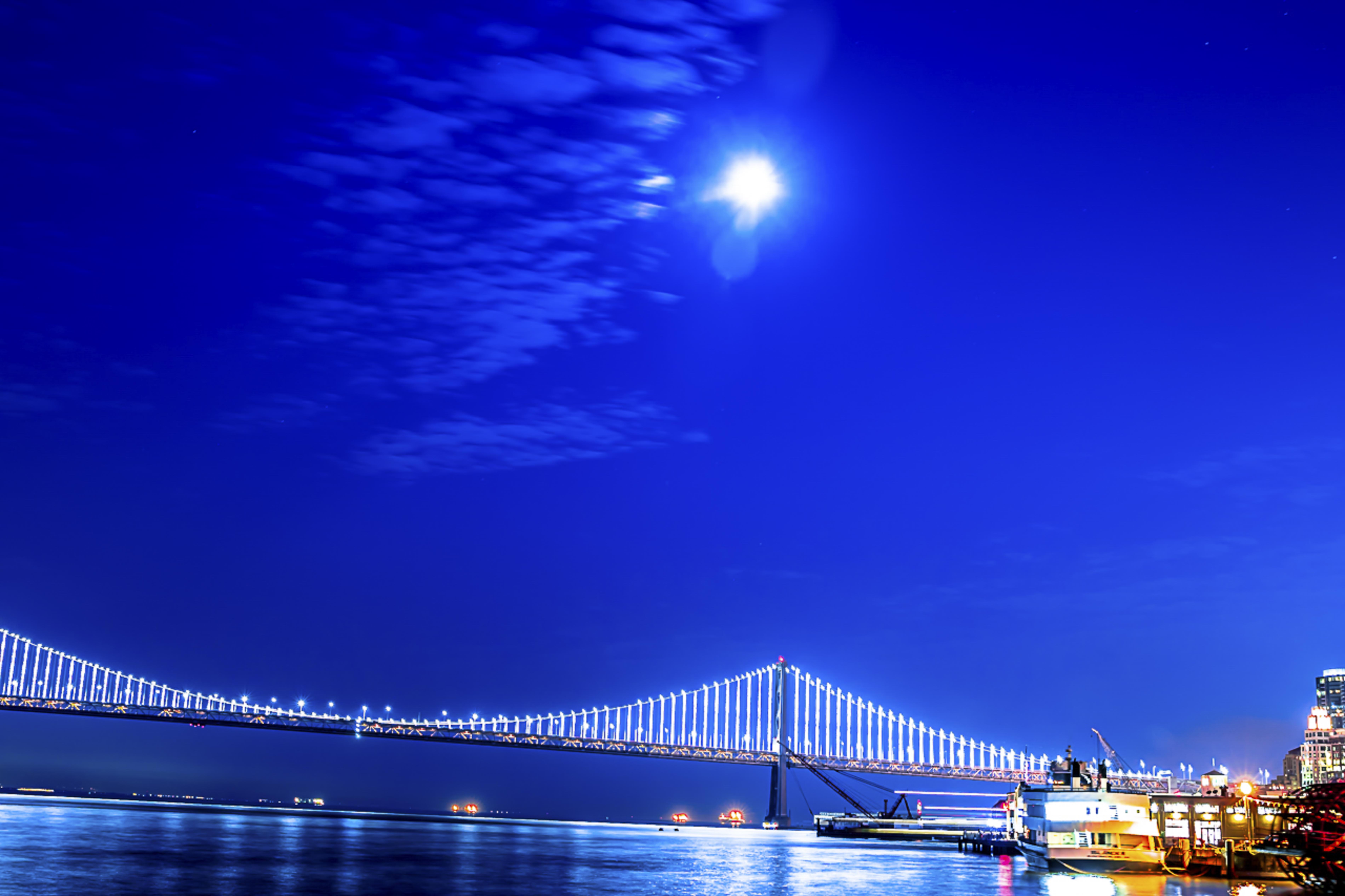 Bay Bridge under a full moon against a deep blue sky