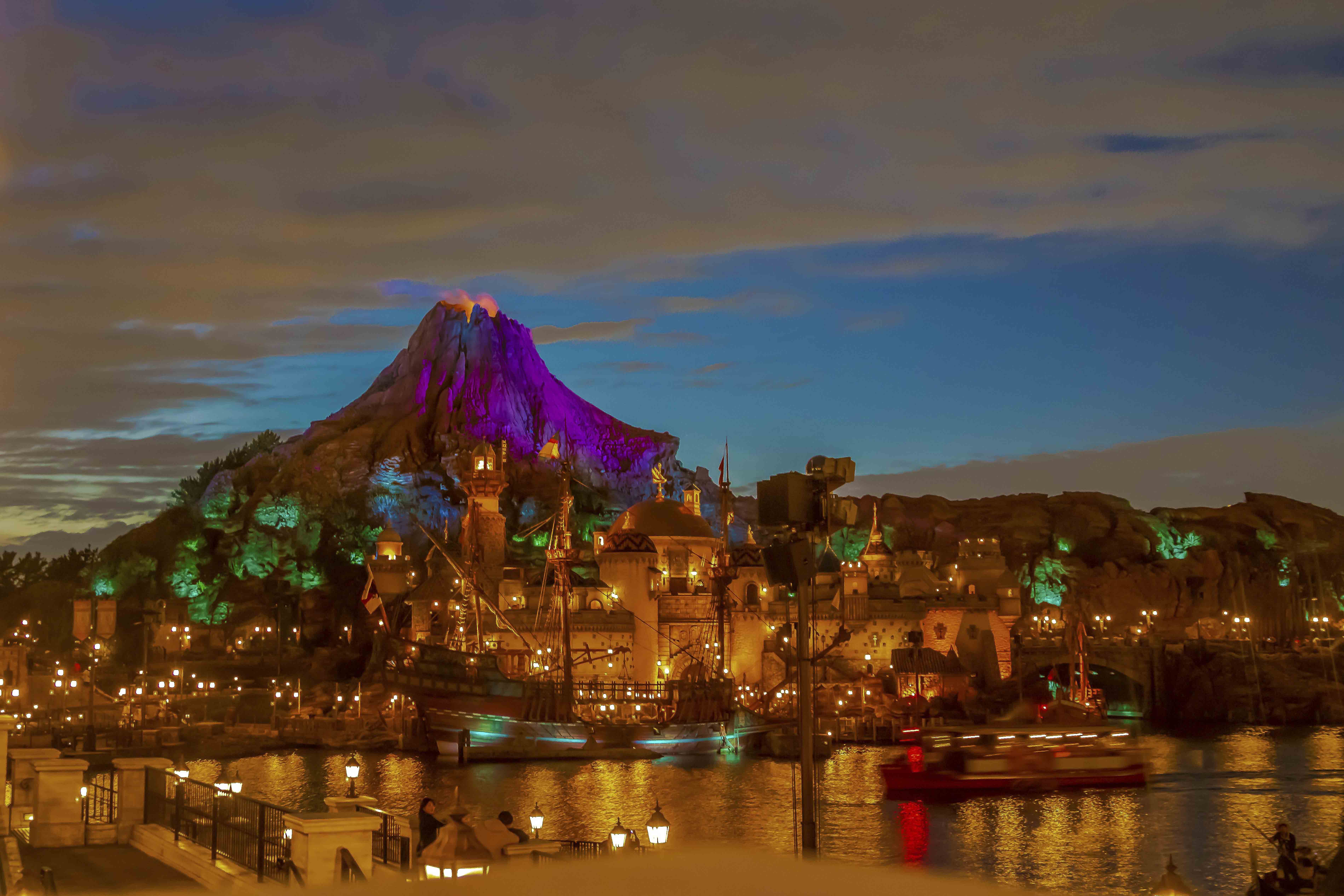 Tokyo DisneySea at night — Mount Prometheus erupts in purple and teal light over the harbor